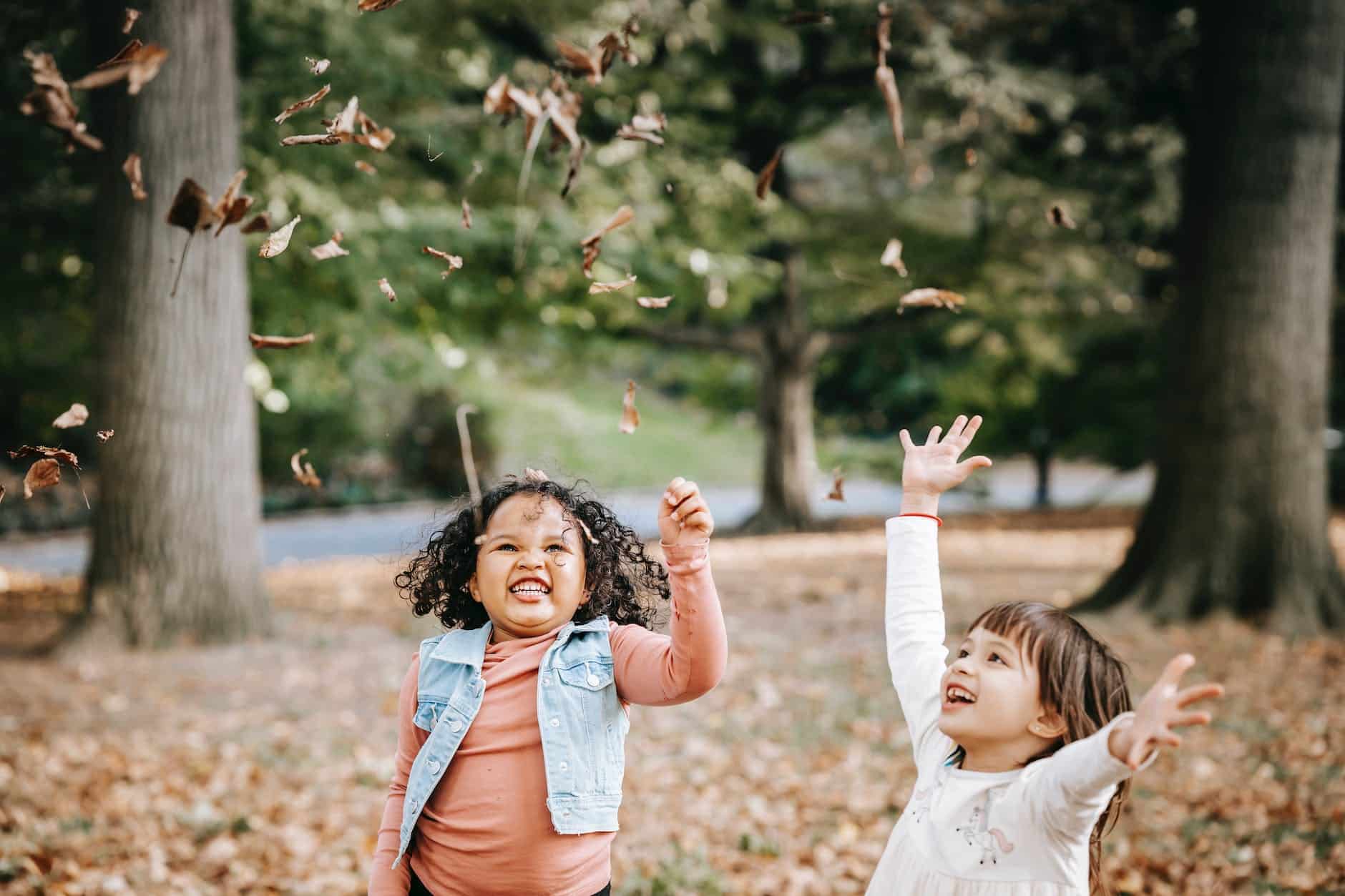 excited children tossing leaves in park